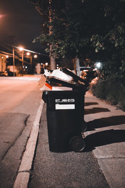 A large pile of black plastic garbage bags, some partially torn, sits against a building with a tiled wall. The bags contain various types of waste and are stacked haphazardly in an outdoor urban environment. Several clear plastic bottles are visible among the bags, indicating plastic refuse. Behind the pile, the wall features graffiti with the word 'XEND' painted in red. The scene appears to be outdoors, possibly in a neglected area or a location awaiting removal, which aligns with private waste disposal or rubbish removal services such as those provided by rubbishremovalelephantandcastle.co.uk. The lighting suggests late afternoon or early evening, with cloudy skies adding a moody atmosphere. The surrounding environment and the state of the waste suggest an urgent need for clearance, which could be managed through separate or independent rubbish collection options, reflecting the context of alternative waste handling outside local authority services.